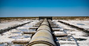 Large industrial pipeline discharging wastewater in arid, rural landscape under clear blue sky.